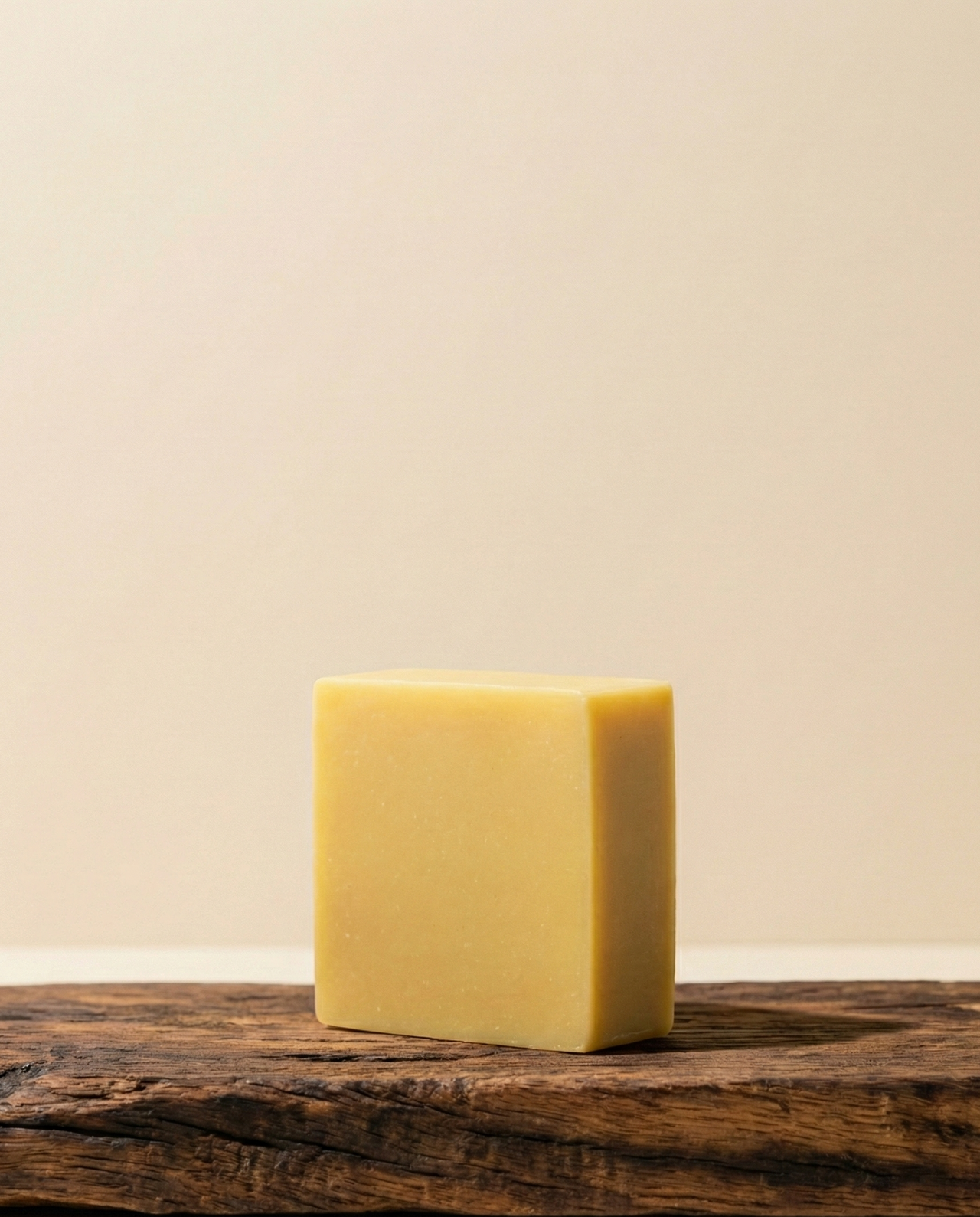 Ochre coloured square soap bar sitting on a darkwood surface with a tan coloured background